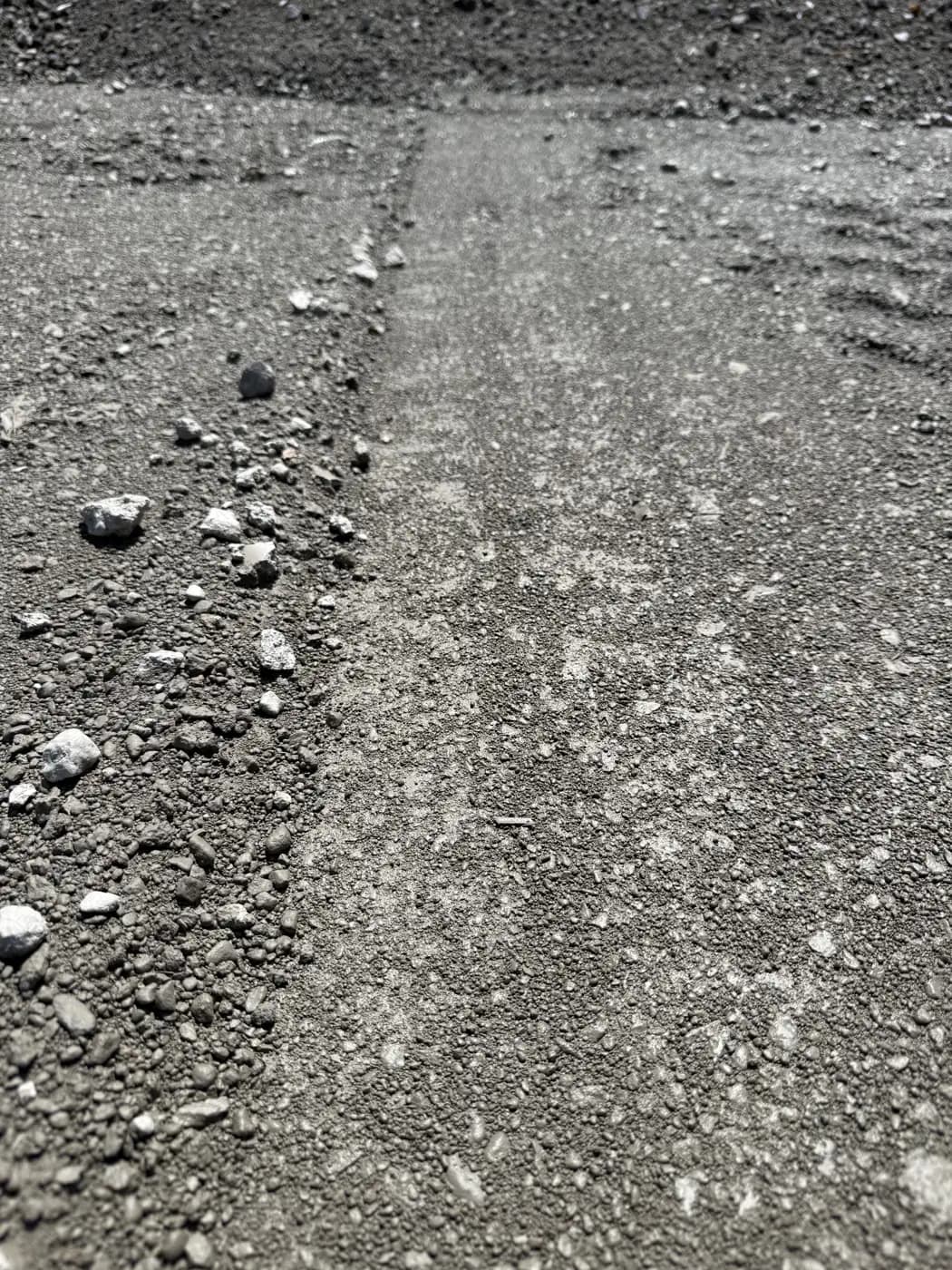Freshly delivered 1½" dense grade gravel — compacted surface beside a raw pile after rain, showing the finished grade GravelRI delivers across Rhode Island